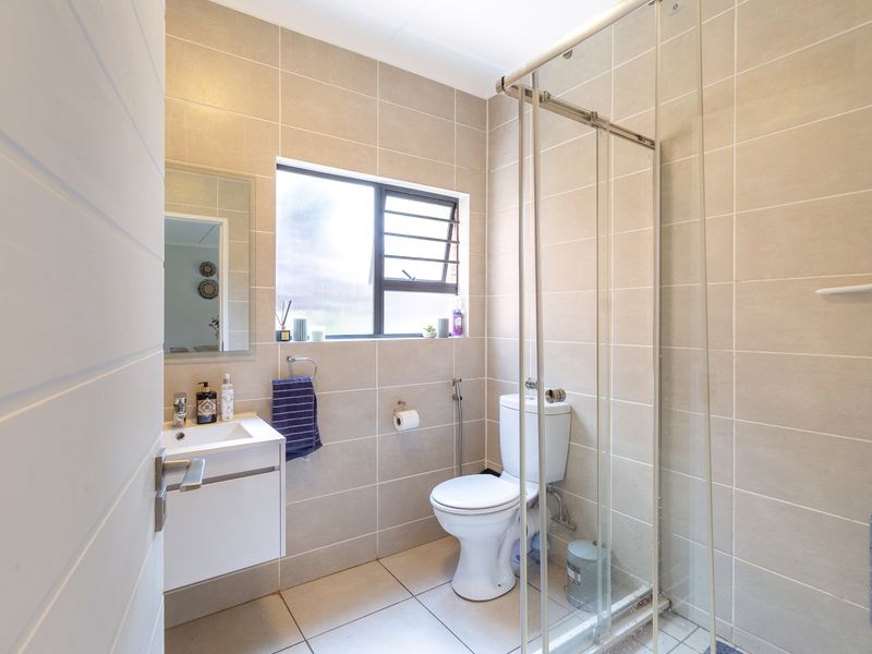 Modern bathroom featuring a vanity with basin, toilet, and a glass-enclosed shower with neutral floor-to-ceiling wall tiles.