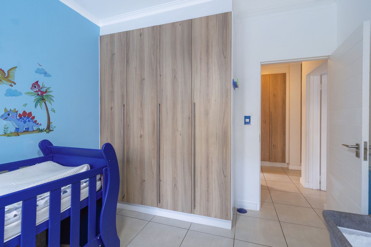 A bedroom featuring modern wood-finish built-in cupboards, tiled flooring, and a bright blue accent wall.