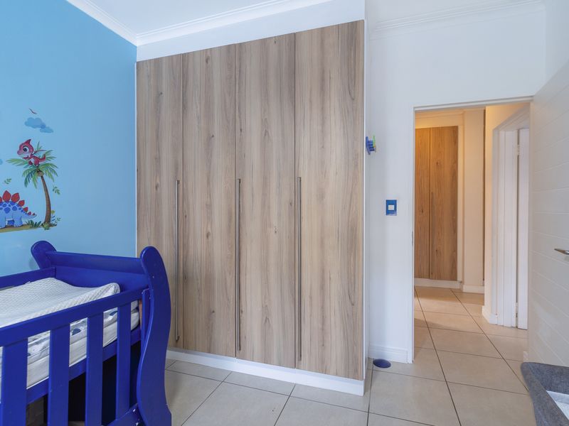 A bedroom featuring modern wood-finish built-in cupboards, tiled flooring, and a bright blue accent wall.