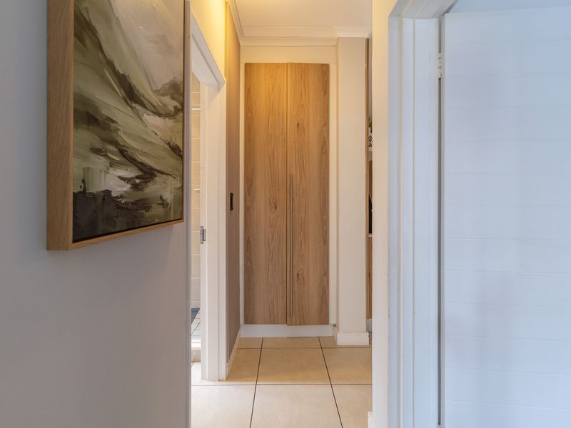 A clean and well-maintained hallway featuring neutral tiled flooring and a modern built-in wooden cupboard.
