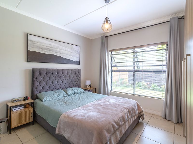 A well-maintained bedroom featuring tiled flooring, a built-in wardrobe, and large windows with venetian blinds, providing ample natural light.
