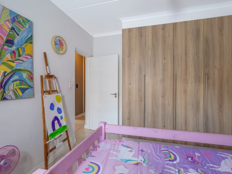 A well-maintained bedroom featuring modern wood-finish built-in cupboards, neutral wall tones, and tiled flooring.