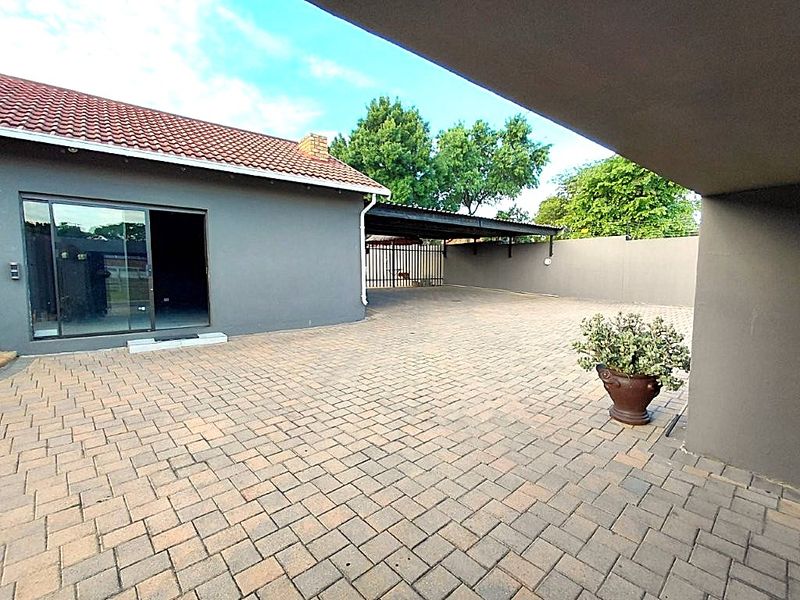 A spacious paved rear courtyard featuring a covered carport, perimeter walling, and direct access to the home via a sliding glass door.