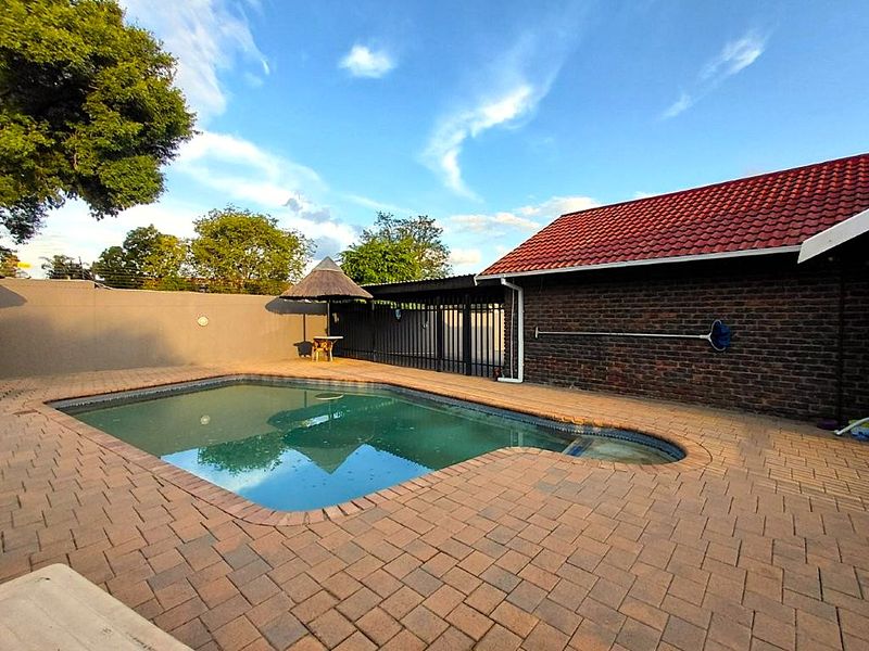 Outdoor pool area featuring brick paving, a swimming pool, and a brick-walled structure with a tiled roof.
