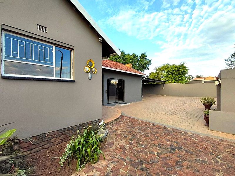 Front exterior view of the property featuring a paved driveway, carport, and secure boundary walling.