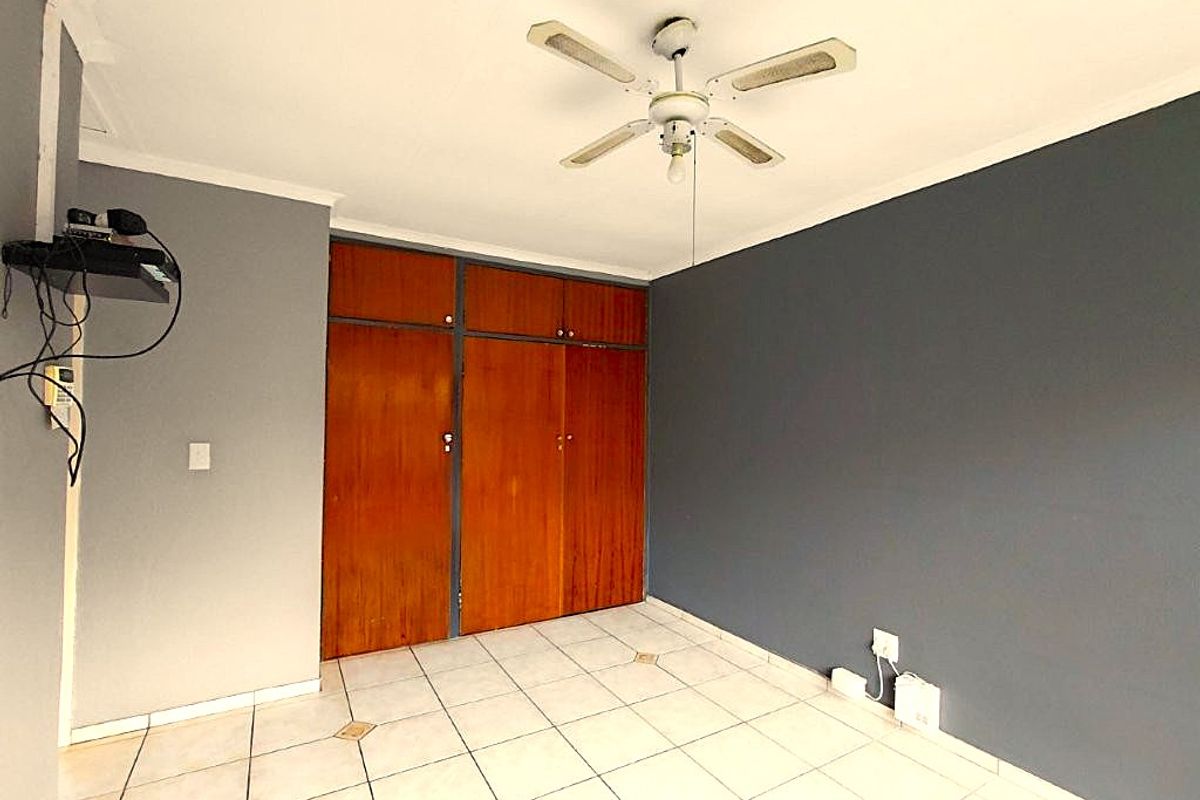 A vacant bedroom featuring tiled flooring, a ceiling fan, and built-in wooden cupboards with a neutral grey wall finish.