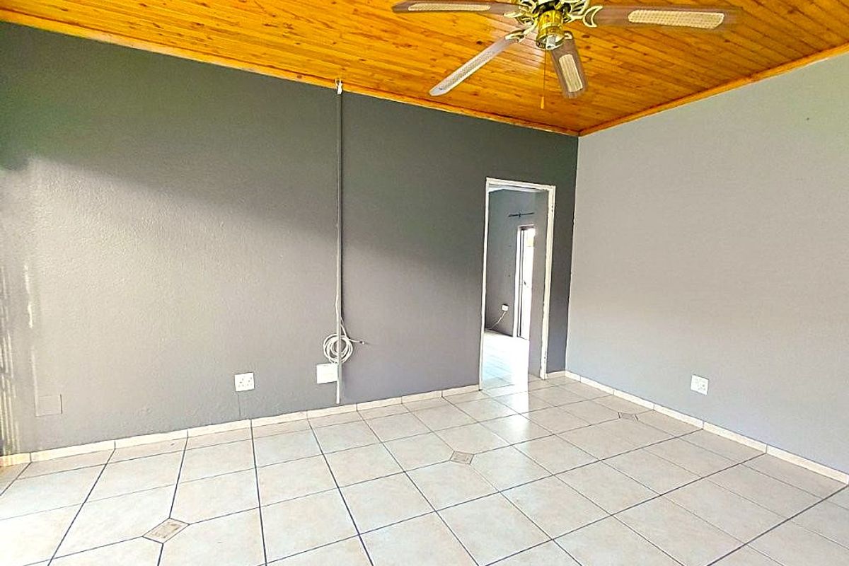 An empty living area featuring a timber ceiling, ceiling fan, and tiled flooring, with an open doorway leading to an adjacent room.