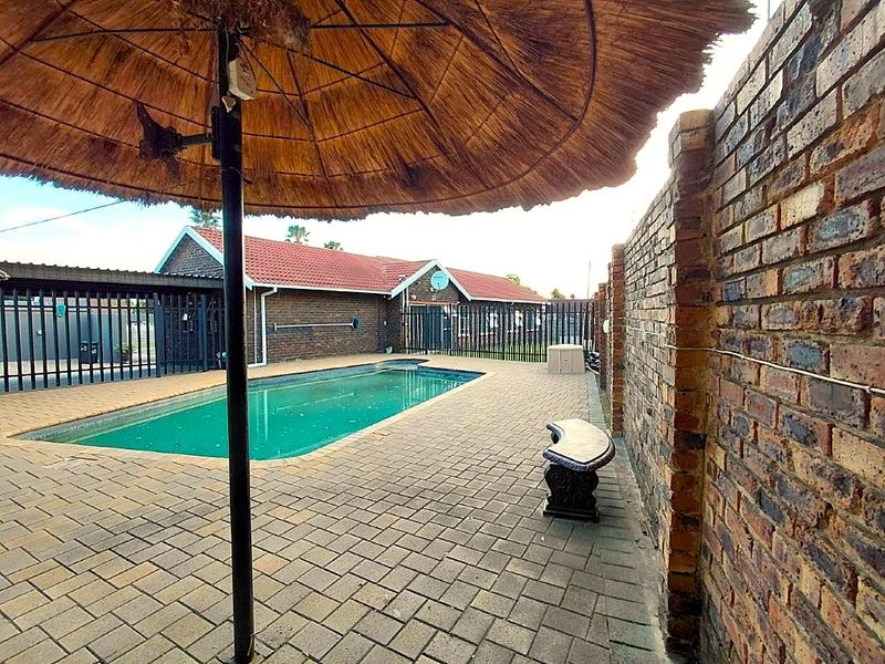 Outdoor pool area featuring a swimming pool, brick paving, and a thatch umbrella, enclosed by a brick boundary wall and metal security fencing.