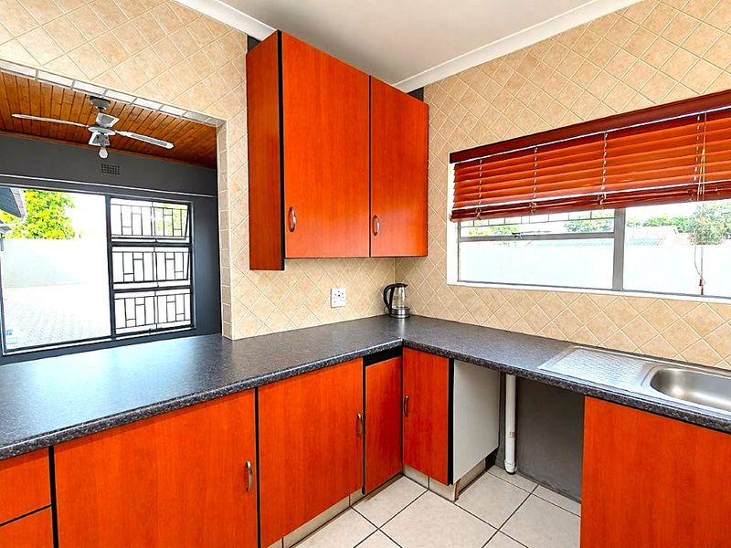 A dated kitchen featuring wood-look cabinetry, tiled backsplash, and a stainless steel sink, requiring minor repairs to cabinetry and plumbing finishes.