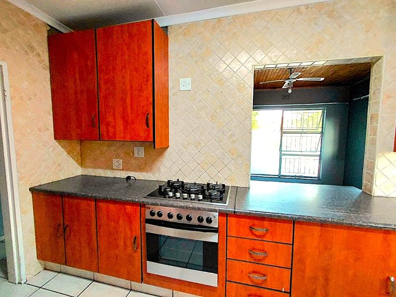 A functional kitchen featuring wood-look cabinetry, a built-in gas hob and oven, tiled backsplash, and a serving hatch opening into the adjacent living area.