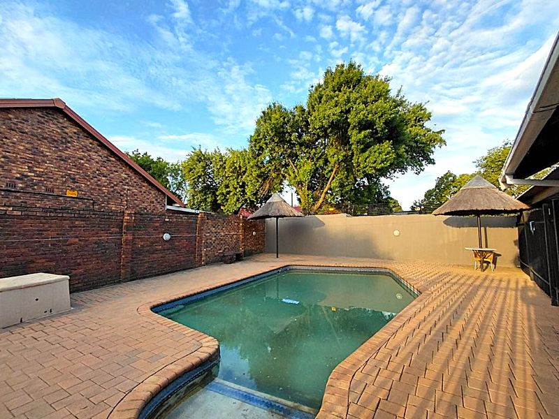 Outdoor pool area featuring a paved deck, brick boundary walls with electric fencing, and two fixed thatched umbrellas.