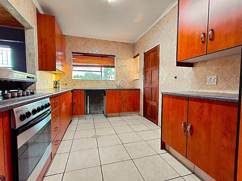 A functional kitchen featuring wooden cabinetry, tiled flooring, and a built-in oven and hob, offering a practical layout with potential for modern updates.