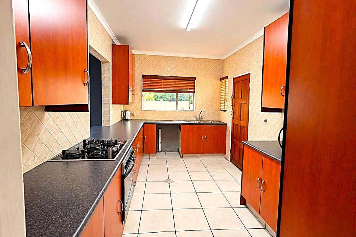 A functional kitchen featuring wood-finish cabinetry, dark laminate countertops, a gas hob, built-in oven, and tiled flooring with a neutral backsplash.