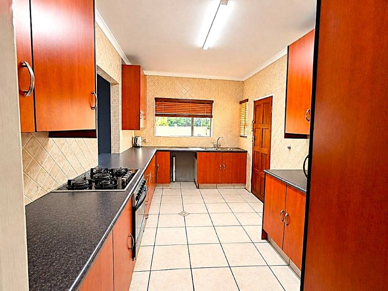 A functional kitchen featuring wood-finish cabinetry, dark laminate countertops, a gas hob, built-in oven, and tiled flooring with a neutral backsplash.