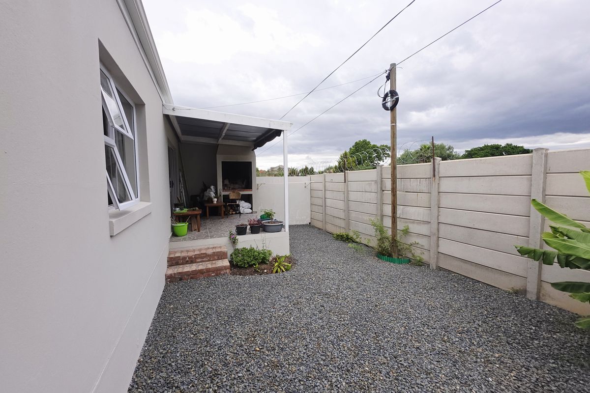 Rear exterior view of the townhouse featuring a covered patio with a built-in braai, gravel garden area, and secure precast boundary walling.