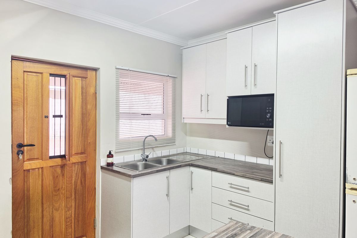A clean and functional kitchen featuring white cabinetry, laminate countertops, a double stainless steel sink, and a built-in microwave with direct exterior door access.