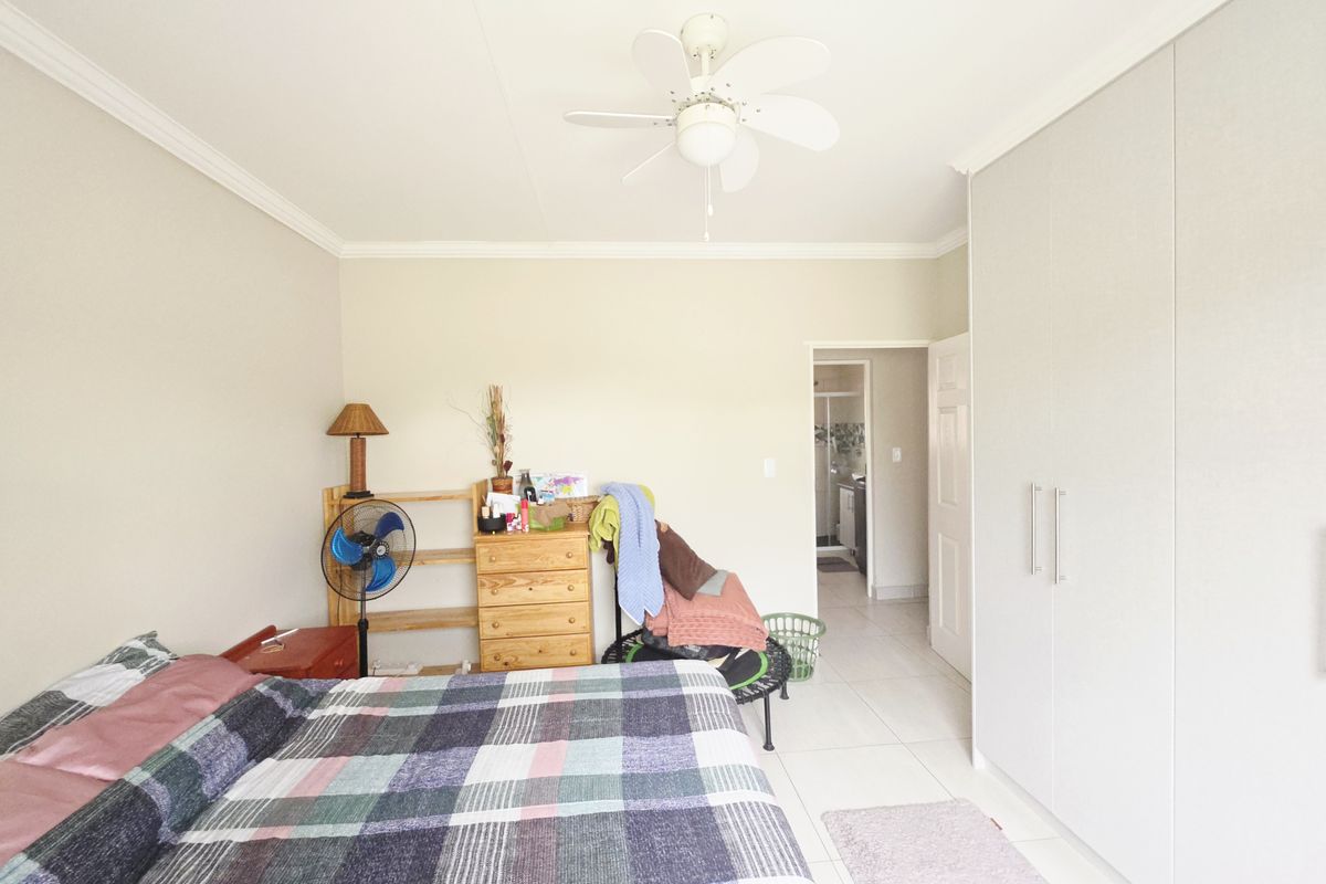 A bedroom featuring built-in cupboards, tiled flooring, and a ceiling fan, with an adjoining en-suite bathroom visible through the doorway.