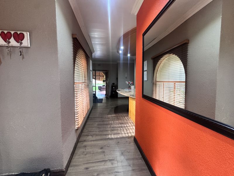 A bright hallway featuring laminate flooring, arched windows with venetian blinds, and recessed ceiling lighting, leading towards an open living area.