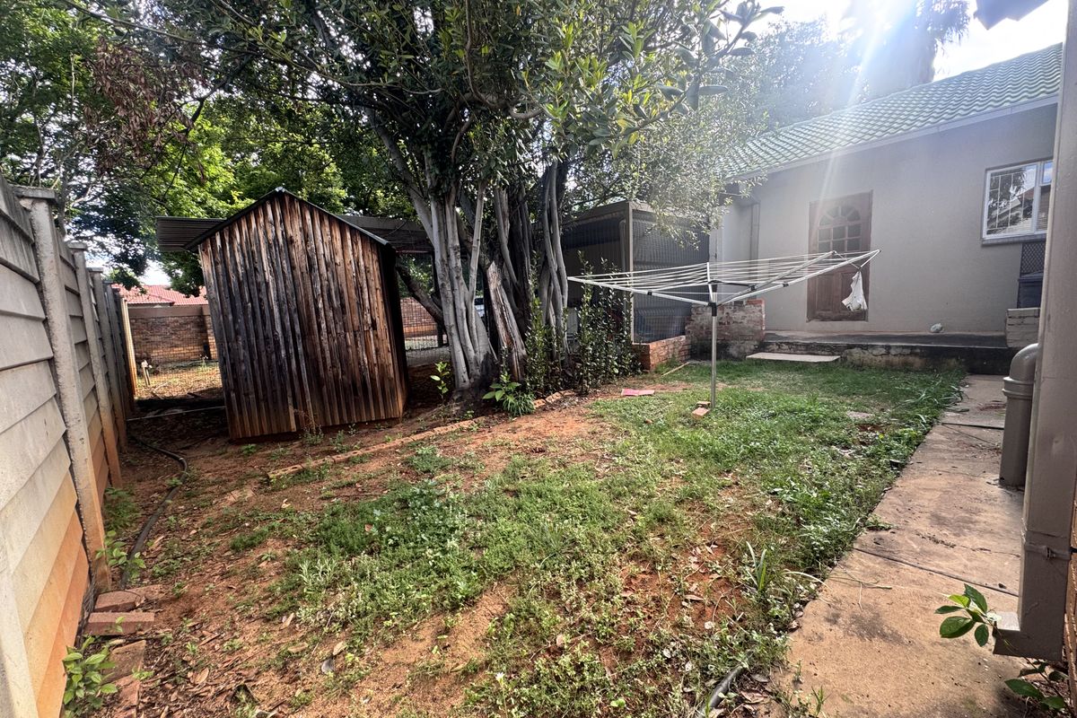 Rear garden area featuring a wooden storage shed, concrete paving, and established trees, offering potential for landscaping and outdoor improvement.