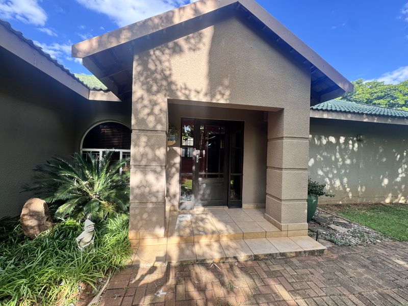 Front entrance of the house featuring a covered tiled porch, stucco facade, and a timber-framed front door with an adjacent arched window.