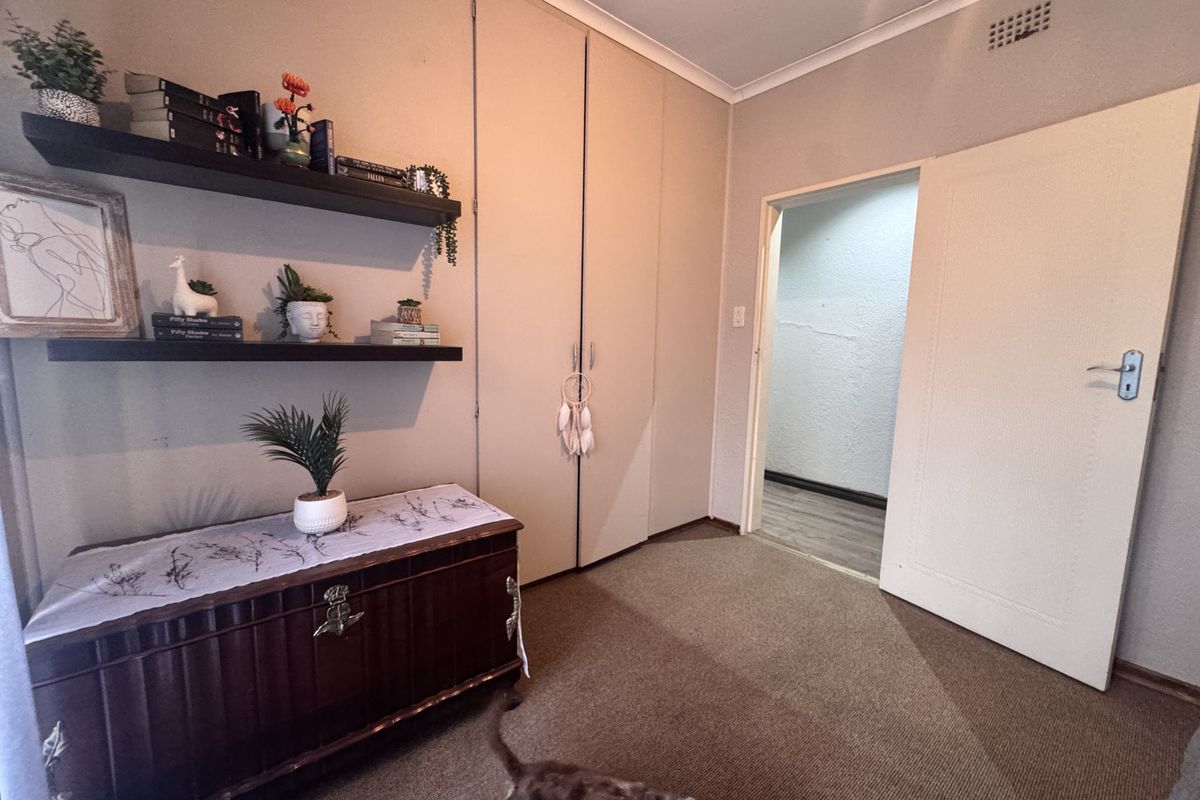 A bedroom featuring built-in cupboards, carpeted flooring, and a ventilation grille, with visible wall plaster cracking near the doorway.