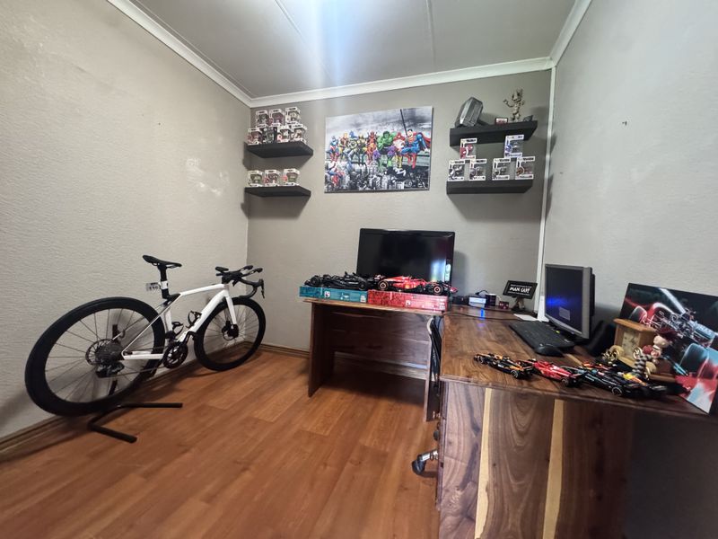 A functional home office space featuring laminate flooring, floating wall shelves, and neutral wall finishes, suitable for a dedicated workspace or study area.