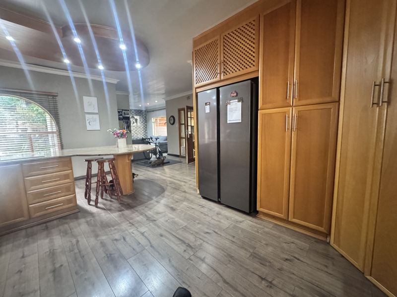 A kitchen area featuring extensive built-in wooden cabinetry, a breakfast bar, and modern laminate flooring with recessed ceiling lighting.