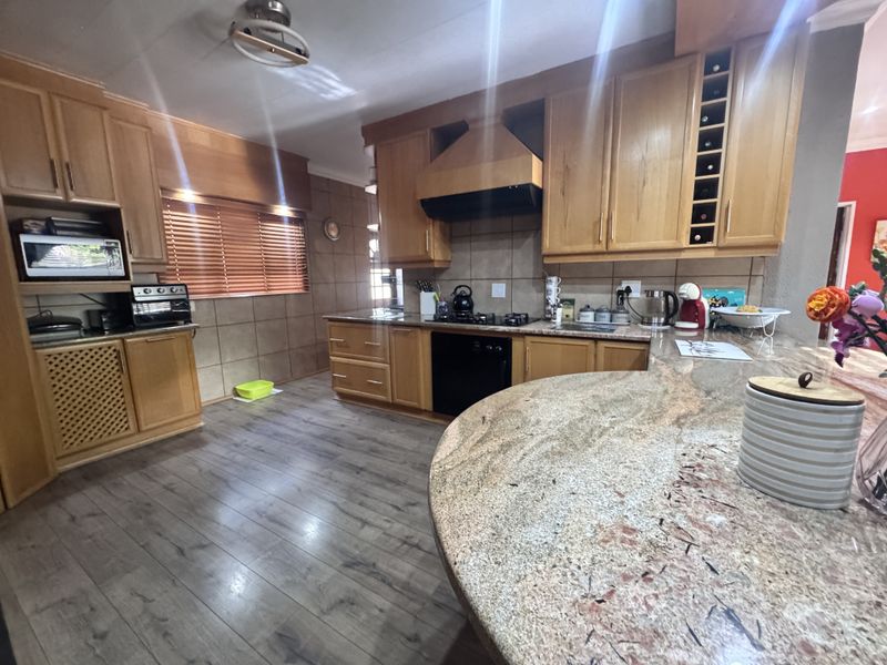 Spacious kitchen featuring warm wooden cabinetry, granite countertops, a gas hob with extractor, and durable laminate flooring, offering a functional and inviting cooking space.