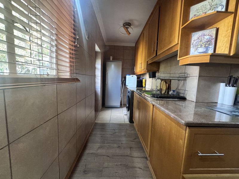 A functional scullery featuring wooden cabinetry, granite countertops, and tiled wall finishes, providing additional workspace and storage adjacent to the main kitchen area.