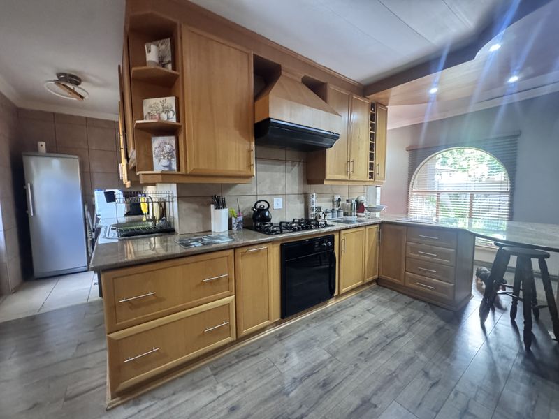 A functional kitchen featuring wooden cabinetry, granite countertops, built-in oven, gas hob, and a distinctive arched window, providing a warm and practical cooking space.