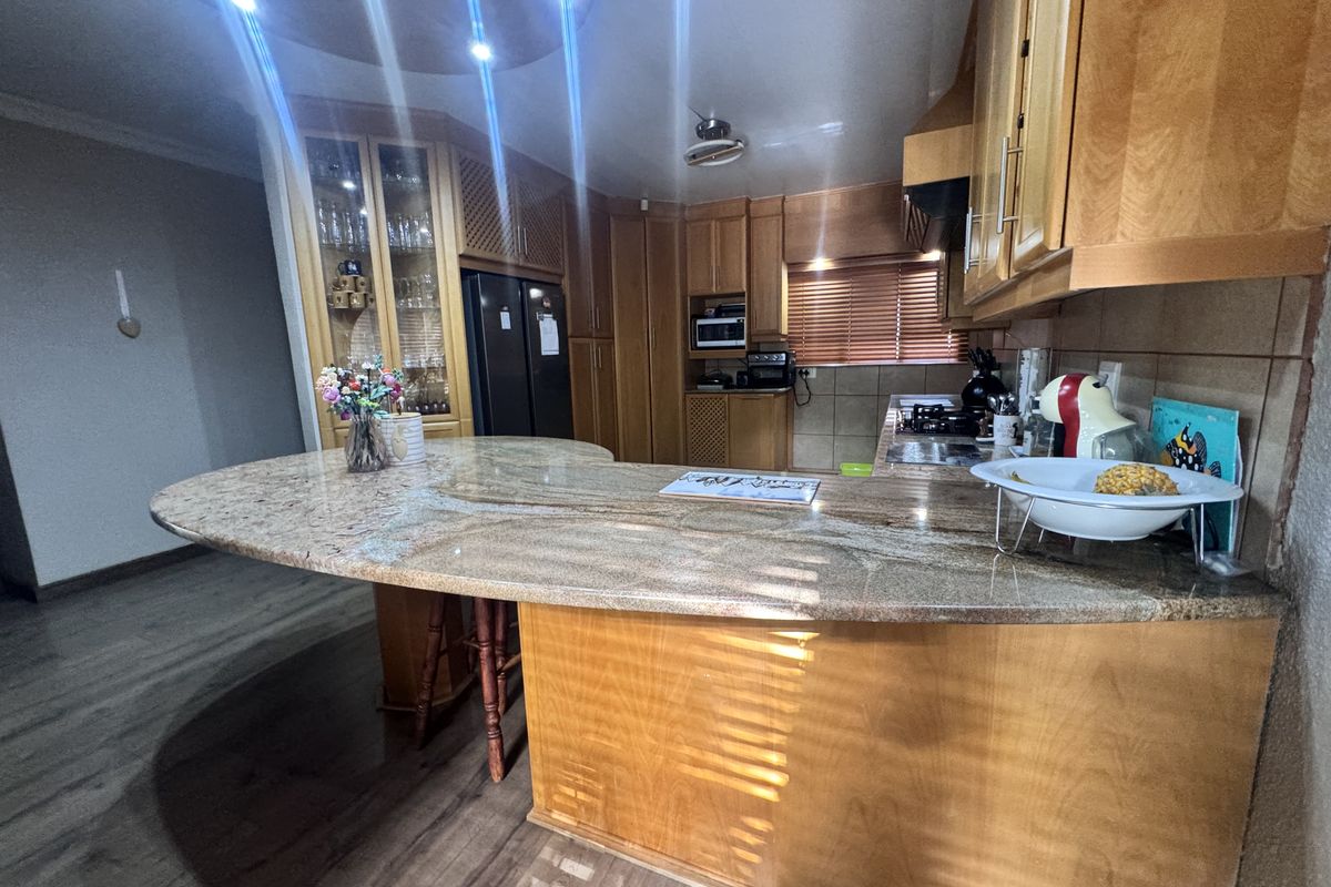 A spacious kitchen featuring extensive wooden cabinetry, a large granite breakfast bar, built-in cooking appliances, and modern recessed lighting.
