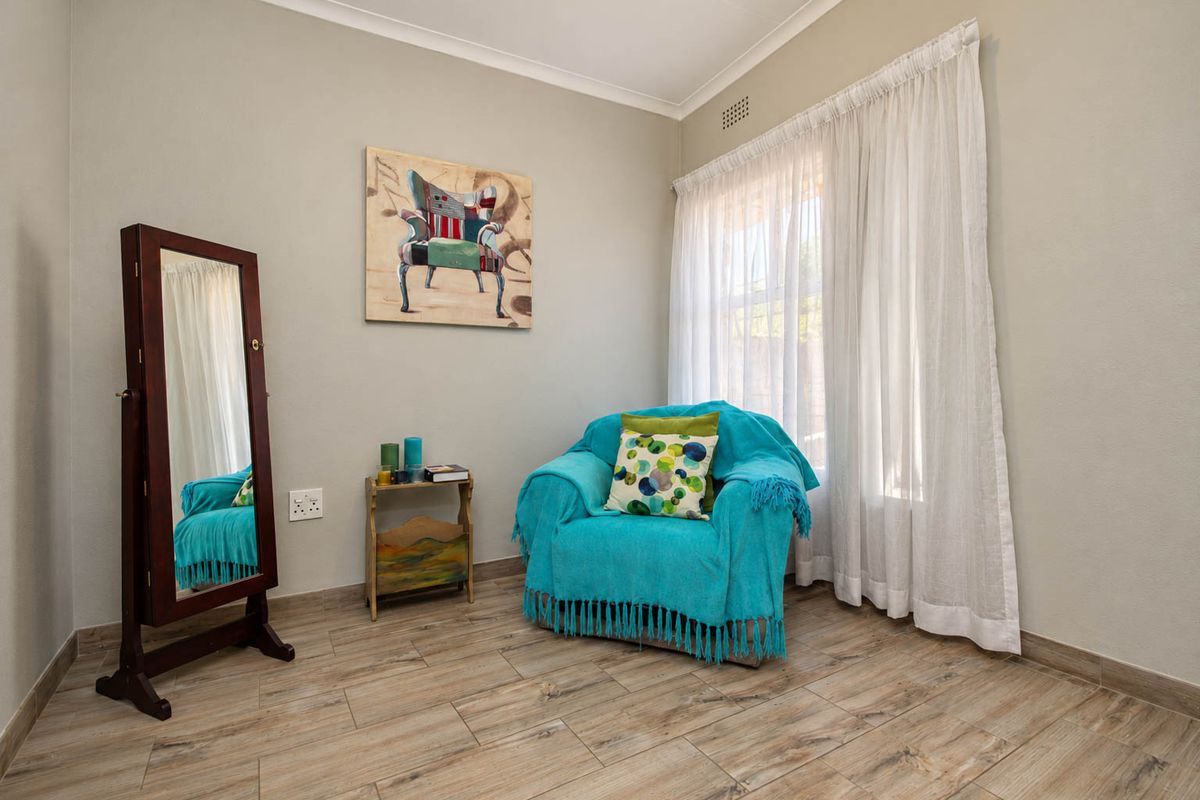 A well-maintained bedroom featuring wood-look tile flooring, neutral wall tones, and natural light through a window with curtain tracks.