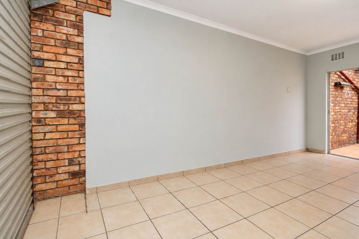 An empty living area featuring ceramic floor tiles, an exposed brick feature wall, and a roller shutter door leading to an outdoor space.