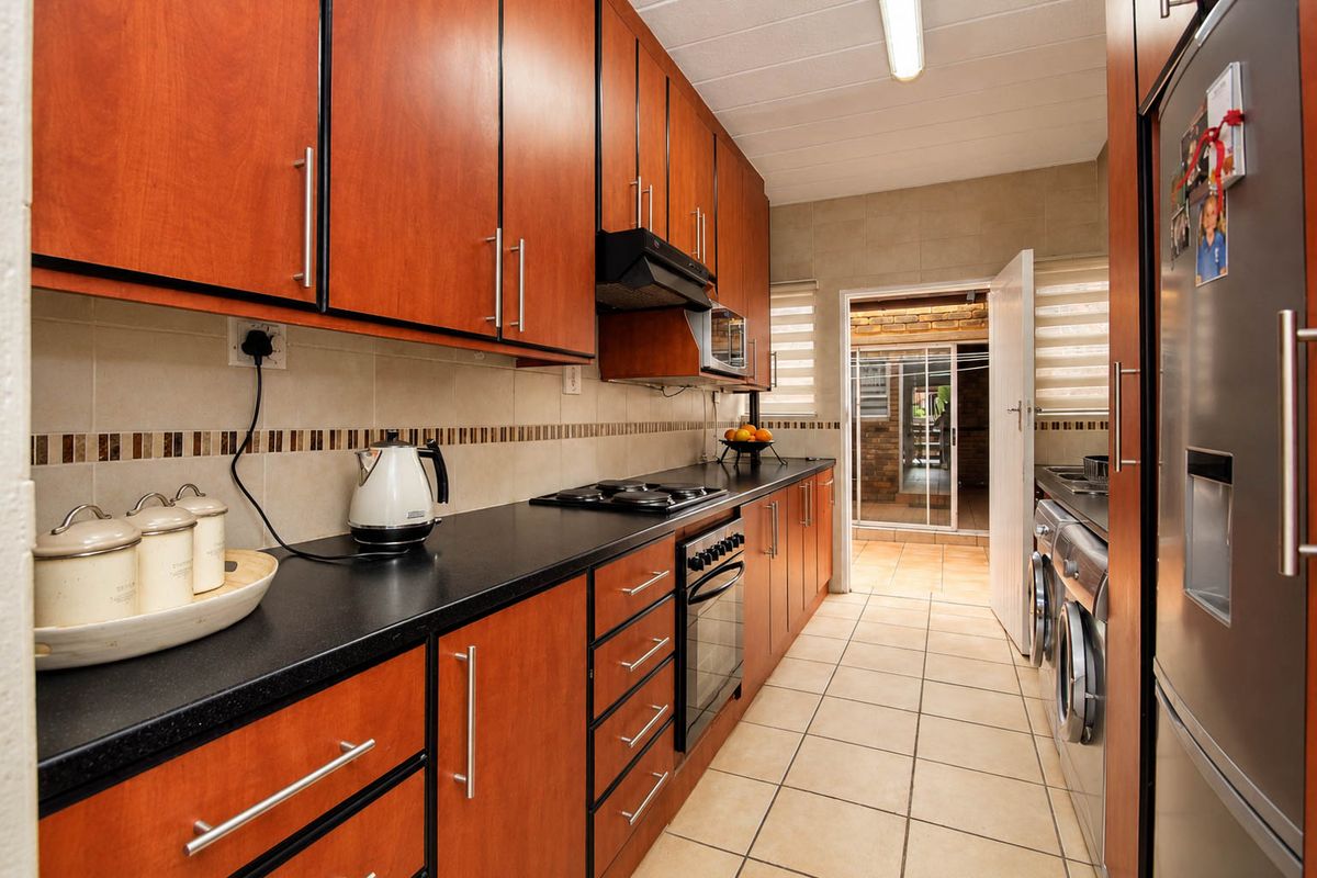 A functional galley-style kitchen featuring wood-finish cabinetry, dark countertops, integrated appliances, and tiled flooring with direct access to an outdoor area.