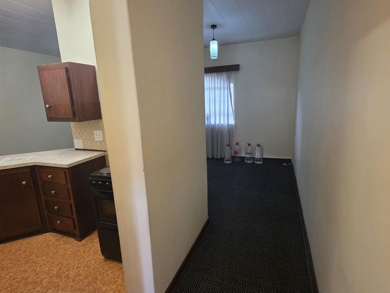 An open-plan living and kitchen area featuring dated cabinetry, a freestanding stove, and contrasting carpet and vinyl flooring, offering a blank canvas for renovation.