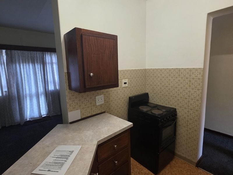 A compact kitchen area featuring dated cabinetry, a laminate countertop, and a freestanding stove with patterned wall tiling.