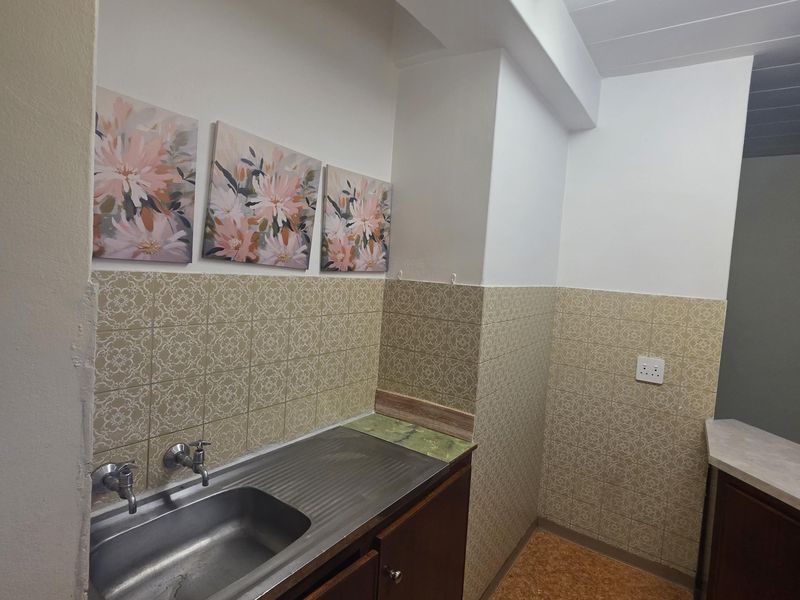 A functional laundry area featuring a stainless steel sink, built-in cabinetry, and tiled splashbacks, offering a practical space for utility tasks.