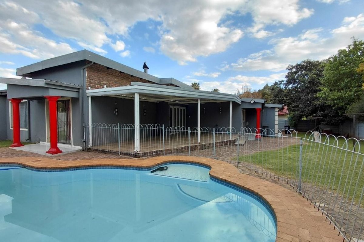 Rear exterior view featuring a swimming pool with brick coping, a covered patio area, and a spacious garden with perimeter fencing.