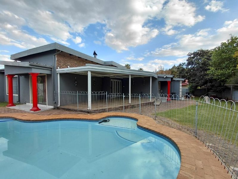 Rear exterior view featuring a swimming pool with brick coping, a covered patio area, and a spacious garden with perimeter fencing.