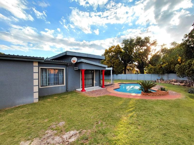 Rear exterior view featuring a swimming pool, brick paved patio area, and a lawned garden with perimeter walling.