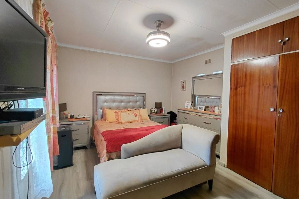 A bedroom featuring laminate flooring, built-in wooden cupboards, and a ceiling fan, with visible signs of ceiling water staining.