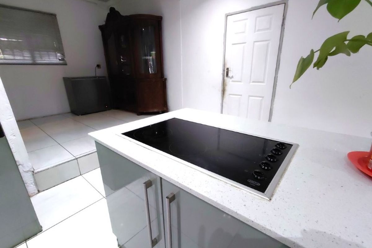 Kitchen area featuring a central island with a built-in electric hob, stone countertops, and tiled flooring, leading to a raised secondary space.