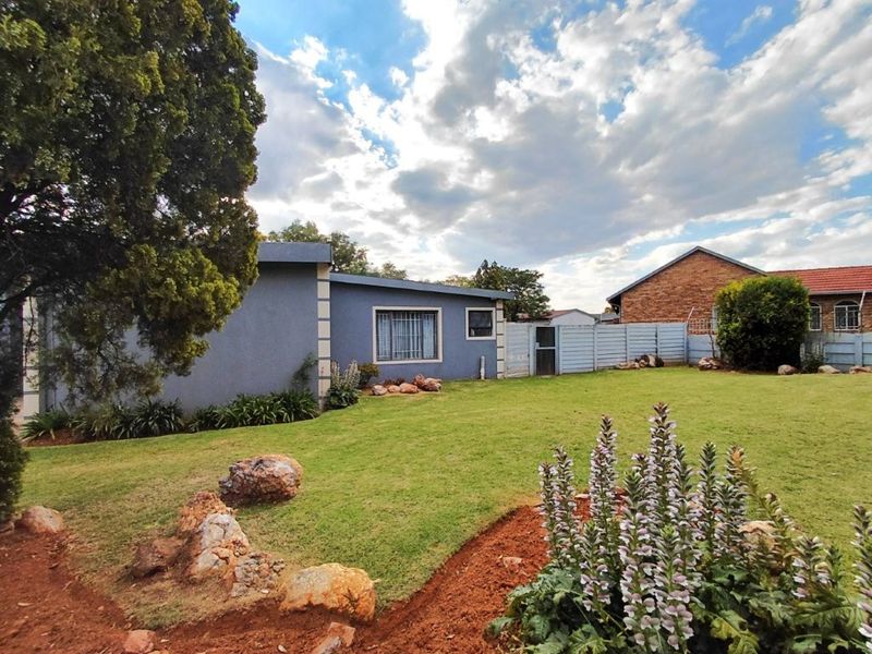 A view of the rear garden featuring a well-maintained lawn, established landscaping, and a secure perimeter wall with a metal gate.