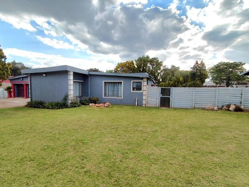 Rear view of the house featuring a spacious lawn, perimeter fencing, and security bars on the windows.