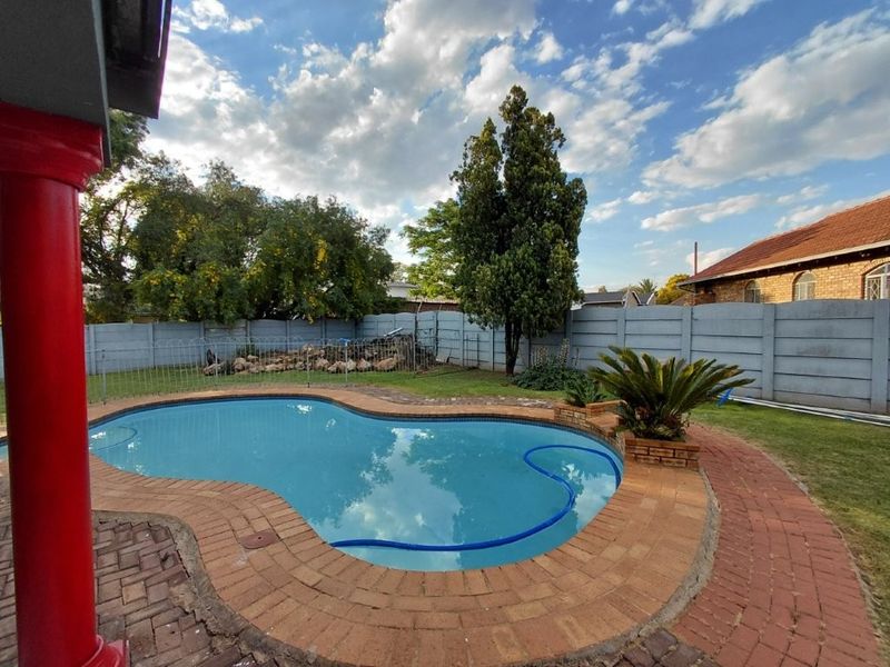 Outdoor pool area featuring a kidney-shaped swimming pool, brick paving surround, and perimeter precast concrete walling.