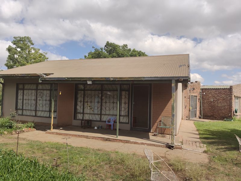 Rear view of a single-story brick house featuring a covered patio, corrugated metal roof, and security-fitted windows and doors.