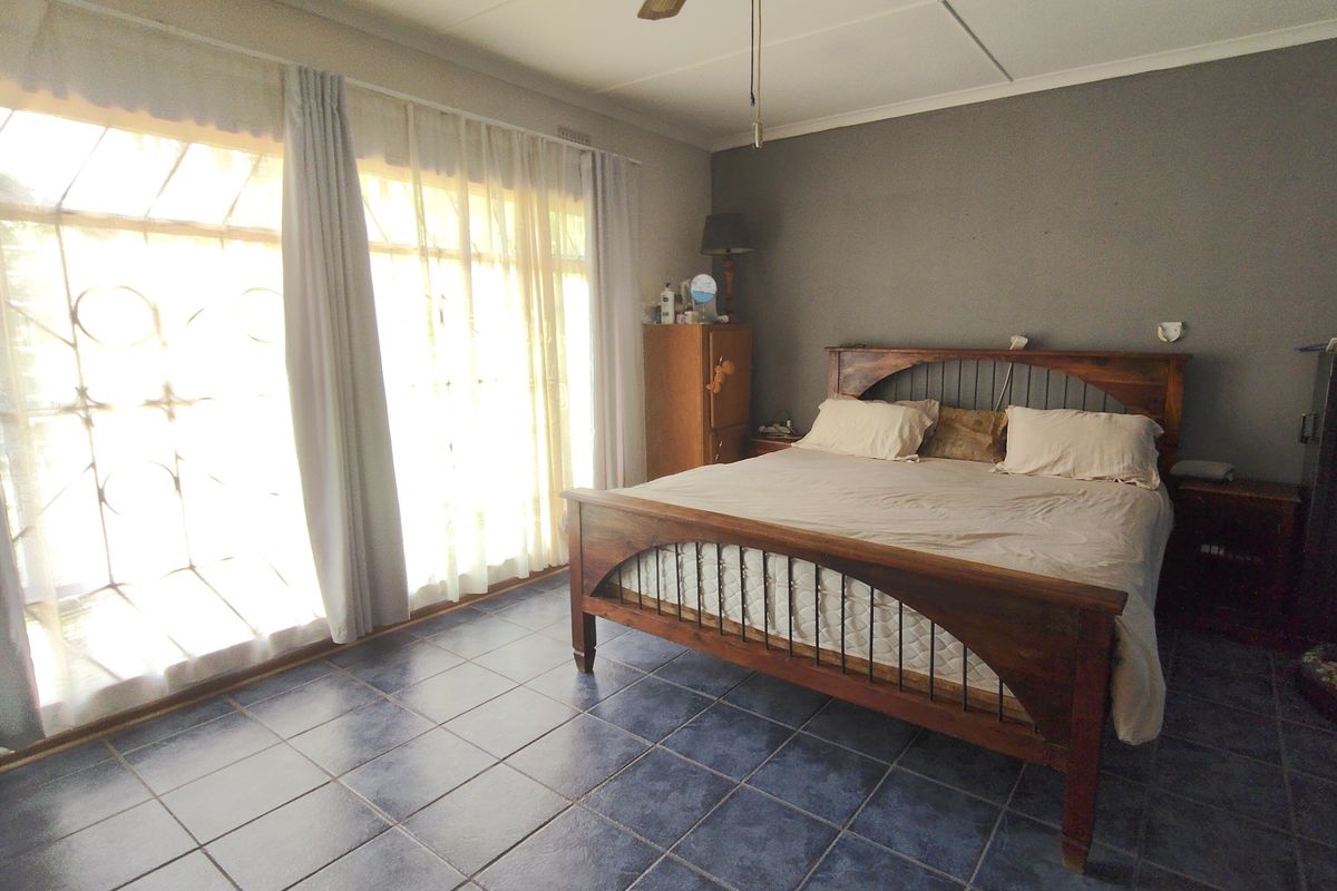 Spacious bedroom featuring dark tiled flooring, a ceiling fan, and large windows with security gates allowing for ample natural light.