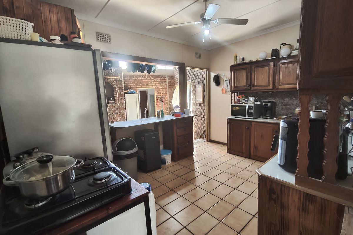 A functional kitchen featuring traditional wooden cabinetry, tiled flooring, and a breakfast counter, opening into an adjacent brick-walled living space.