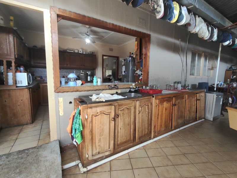 A functional scullery area featuring wooden cabinetry, a stainless steel sink, and a convenient pass-through window connecting to the main kitchen space.