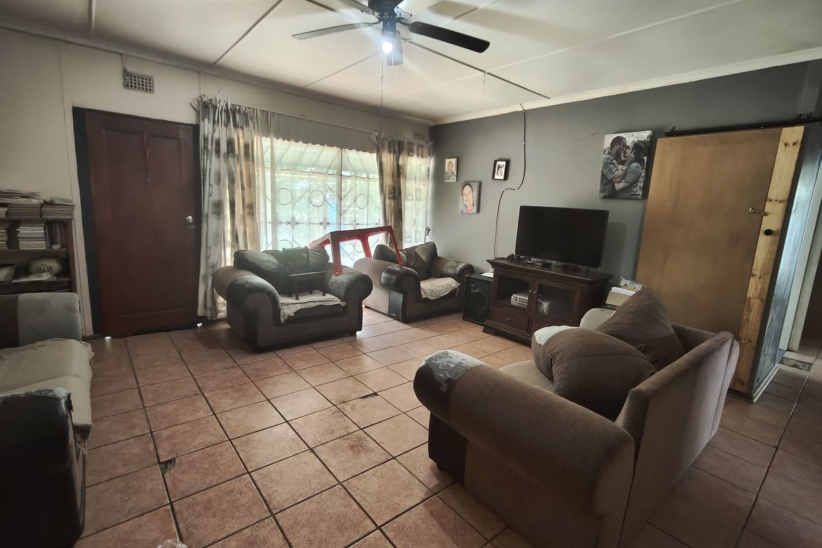 A living room featuring tiled flooring, a ceiling fan, and a sliding door with security gate, requiring cosmetic updates to improve the overall condition.